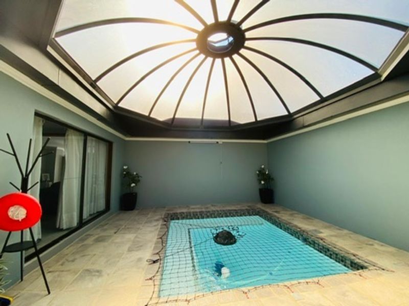 An indoor swimming pool area featuring a large domed skylight, tiled flooring, and sliding glass doors providing access to the main living space.