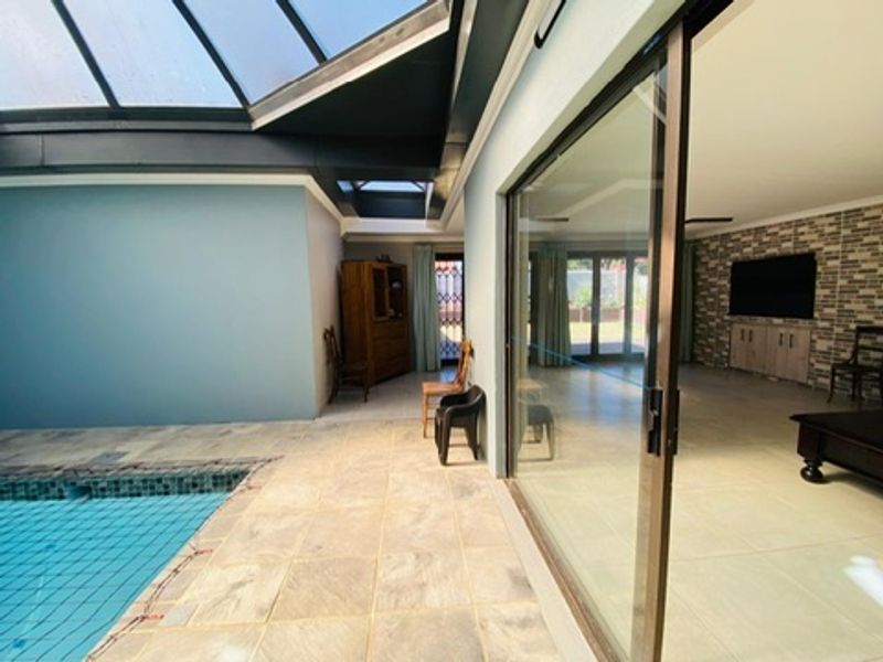 Indoor swimming pool area featuring a large skylight, tiled flooring, and sliding glass doors connecting to the adjacent living space.