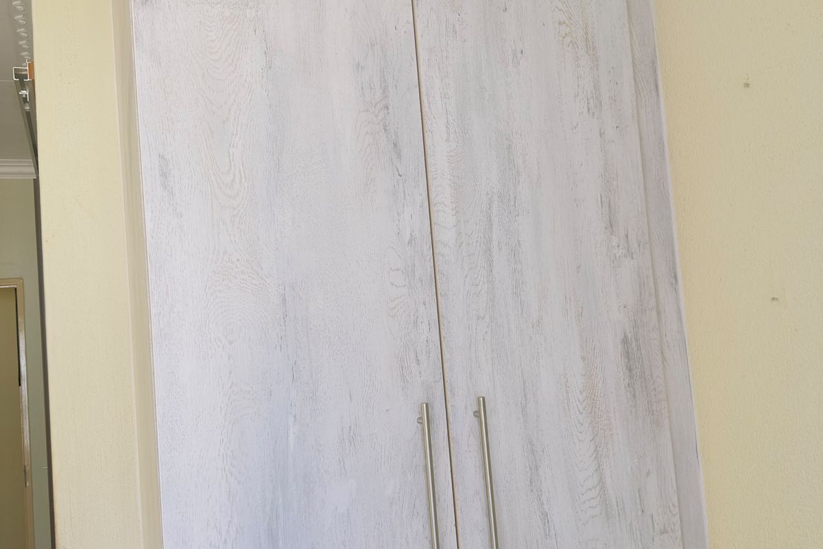 A bedroom featuring a tall, light-wood finish built-in wardrobe with modern handles and decorative ceiling cornicing.