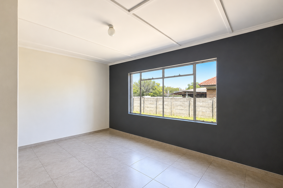 A bright, empty living room featuring neutral tiled flooring, a large window with natural light, and a modern dark accent wall.