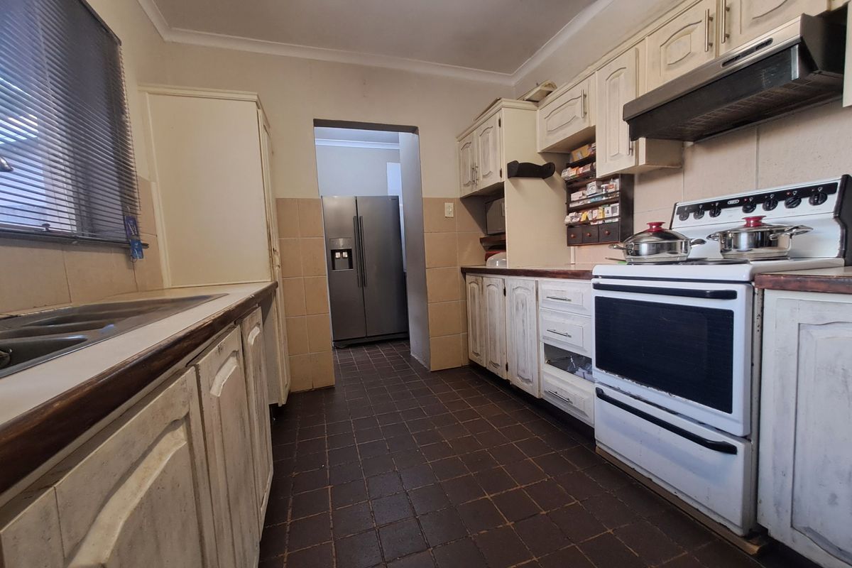 A functional kitchen featuring traditional cabinetry, a freestanding stove with extractor fan, and tiled flooring, offering potential for a modern renovation.