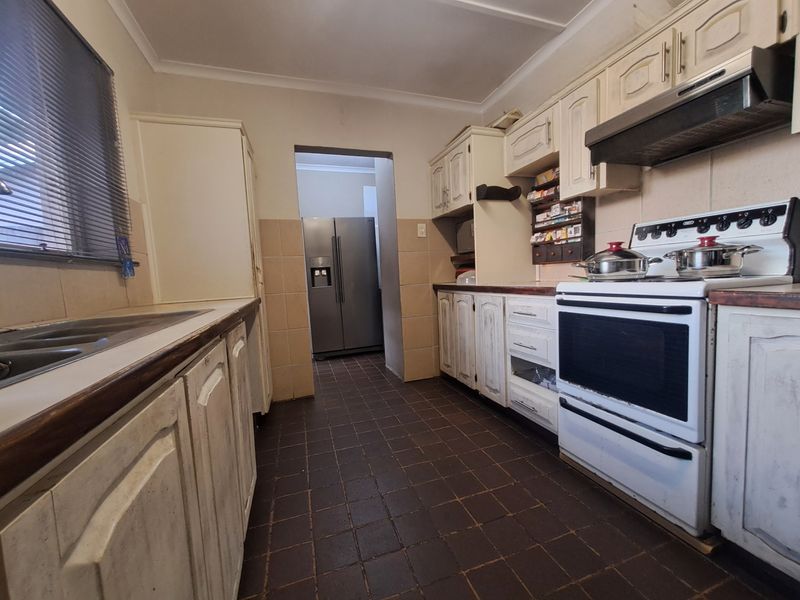 A functional kitchen featuring traditional cabinetry, a freestanding stove with extractor fan, and tiled flooring, offering potential for a modern renovation.