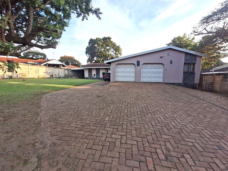 Front view of the property featuring a double garage, extensive paved driveway, and a well-maintained lawn area.