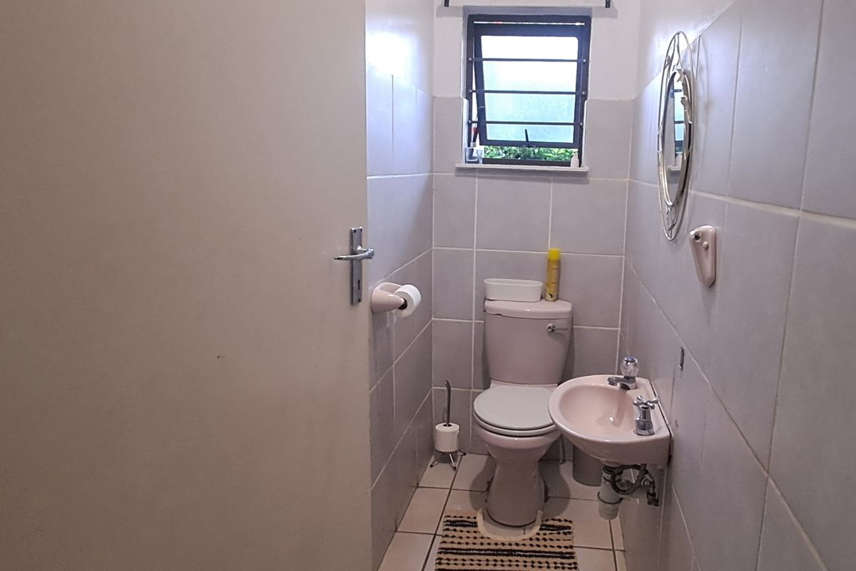 A compact guest bathroom featuring a wall-mounted basin, toilet, and neutral tiled finishes throughout.