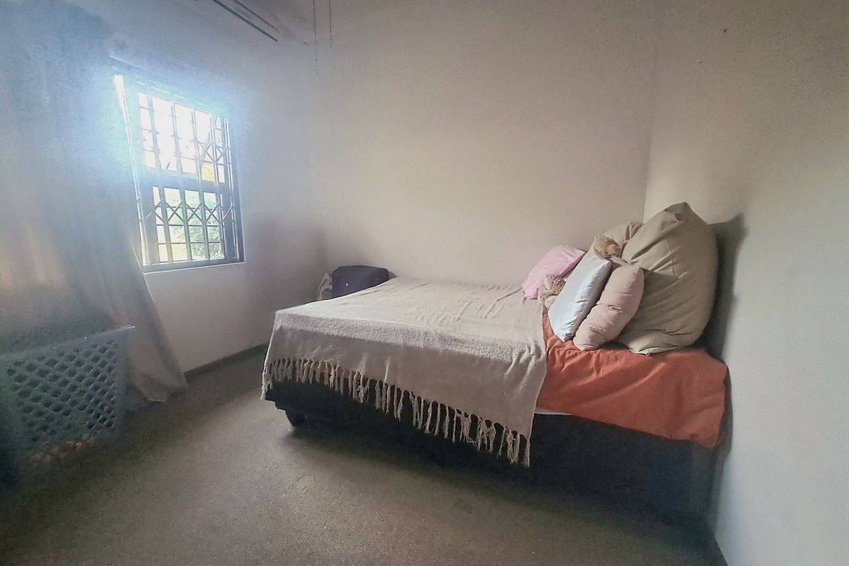 A simple bedroom featuring a window with security bars and a wall-mounted air conditioning unit.