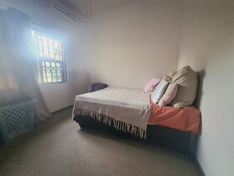 A simple bedroom featuring a window with security bars and a wall-mounted air conditioning unit.