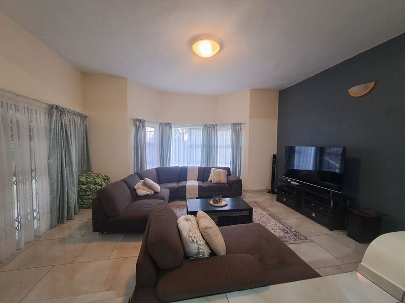 A spacious living room featuring large tiled floors, a bay window, and a dark accent wall, providing a comfortable and functional family living space.