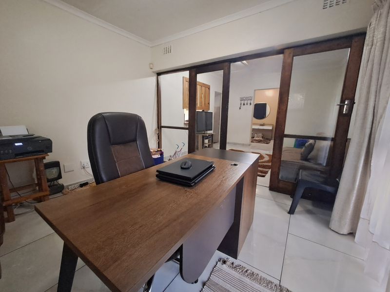 A functional home office space featuring tiled flooring and large sliding glass doors that provide a view into the adjacent living area.