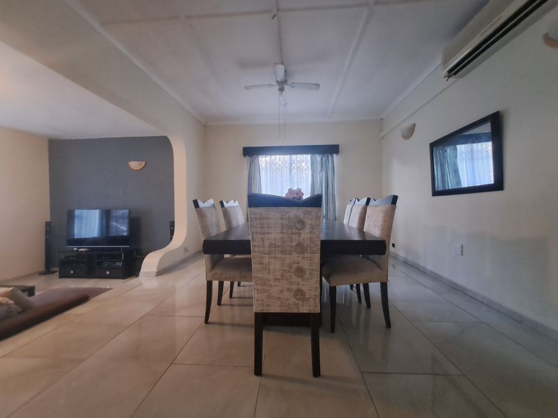 Open-plan living and dining area featuring tiled flooring, a ceiling fan, and a distinctive arched wall partition.
