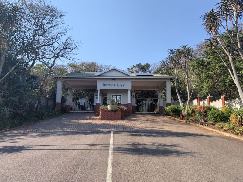 The main entrance gate to Abrams Crest, featuring a paved driveway, security guard house, and well-maintained landscaping.