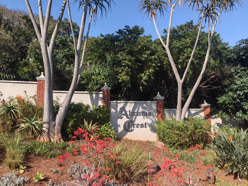 A well-maintained entrance wall and landscaped garden area featuring brick pillars and estate signage for Abrams Crest.