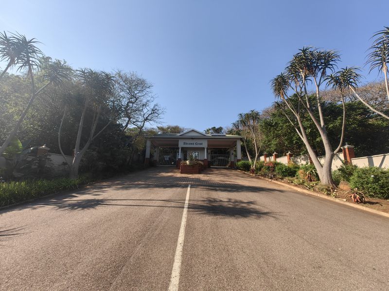 The entrance to Abrams Crest featuring a paved driveway, secure gated access, and well-maintained landscaped surroundings.