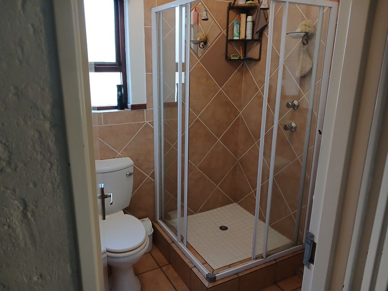 A functional bathroom featuring a corner shower enclosure, toilet, and neutral-toned wall and floor tiling.