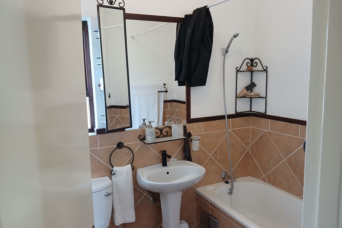 A functional bathroom featuring a pedestal basin, bathtub with handheld shower attachment, and neutral tiled splashbacks.