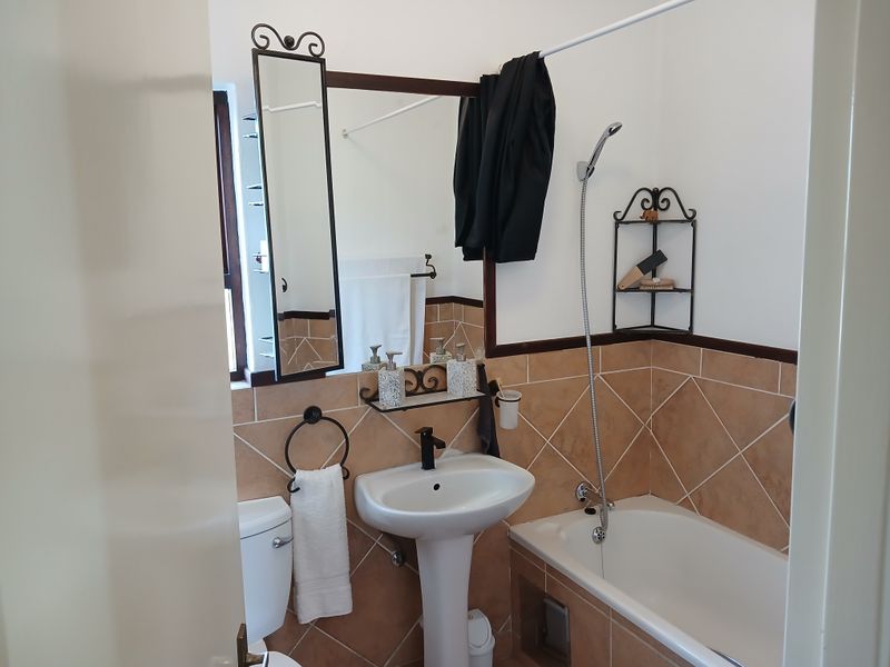A functional bathroom featuring a pedestal basin, bathtub with handheld shower attachment, and neutral tiled splashbacks.