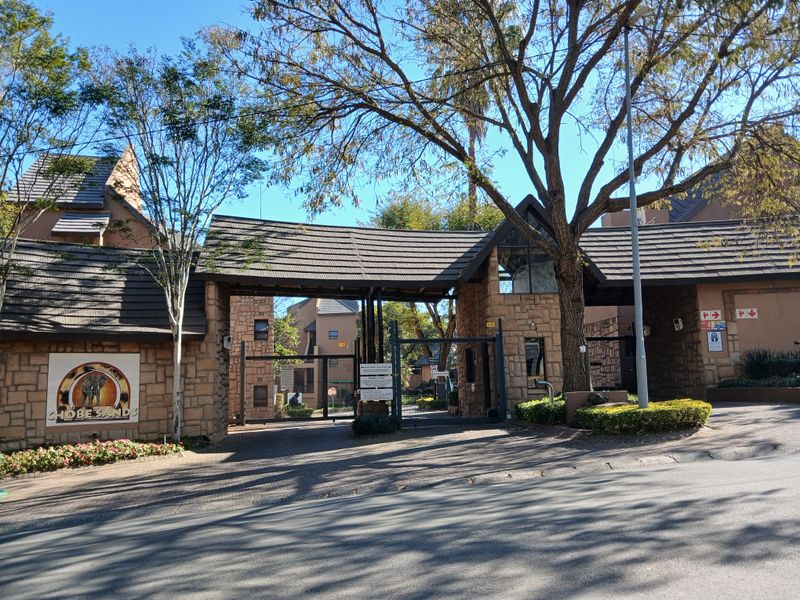 Front entrance view of Chobe Sands complex featuring stone-clad gatehouse, security infrastructure, and mature trees.