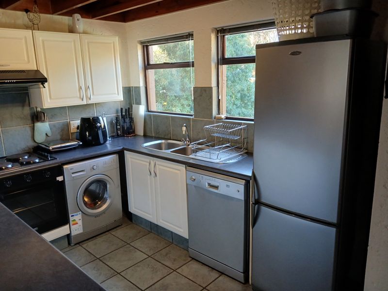 A functional kitchen featuring white cabinetry, tiled backsplash, exposed timber ceiling beams, and integrated appliances including an oven and extractor fan.