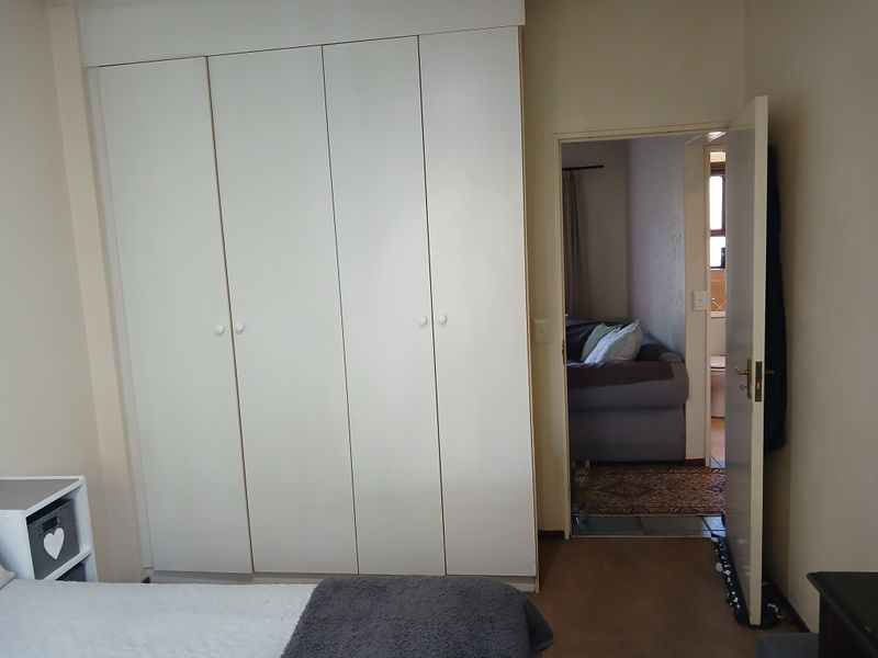 A bedroom featuring a large white built-in wardrobe with a doorway leading to an adjacent room.
