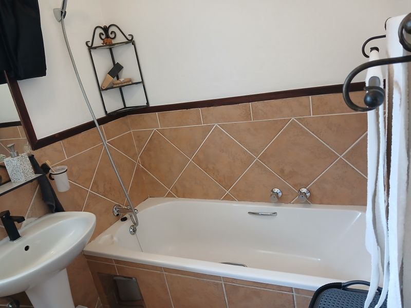 A functional bathroom featuring a pedestal basin, a bathtub with a shower mixer, and neutral-toned wall tiling.