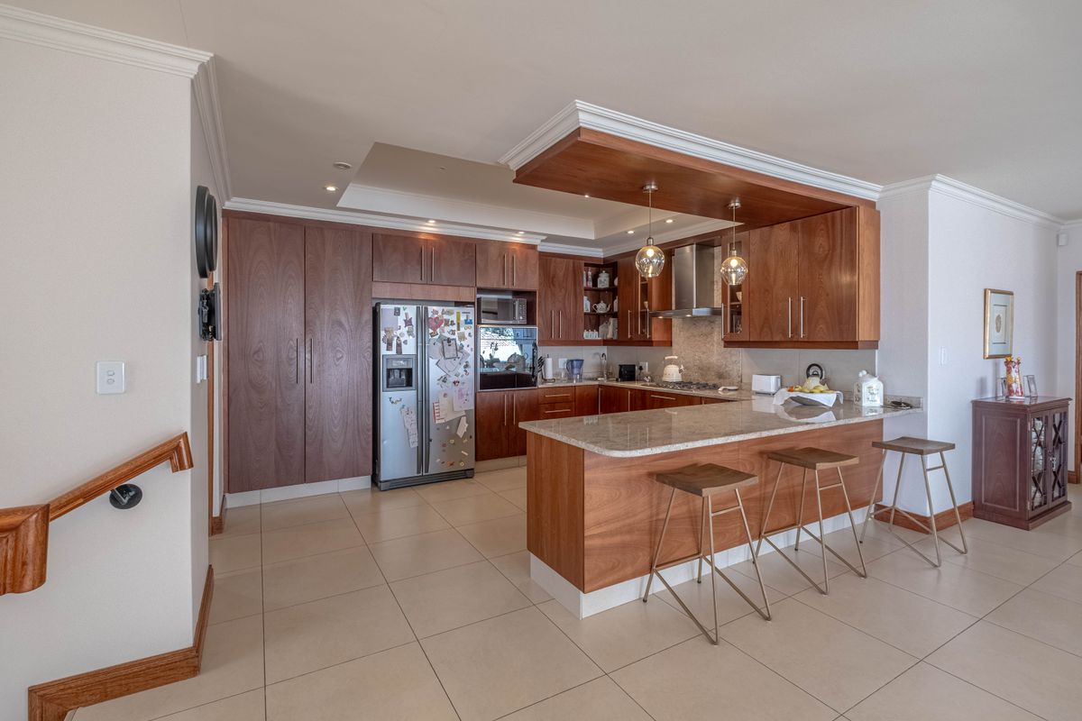 Modern kitchen featuring rich wooden cabinetry, granite countertops, a breakfast bar, and integrated appliances, complemented by recessed lighting and tiled flooring.