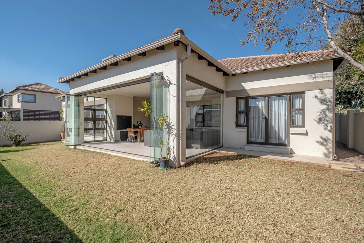 Rear view of the property featuring a covered patio with stacking glass doors, a built-in braai, and a well-maintained garden.