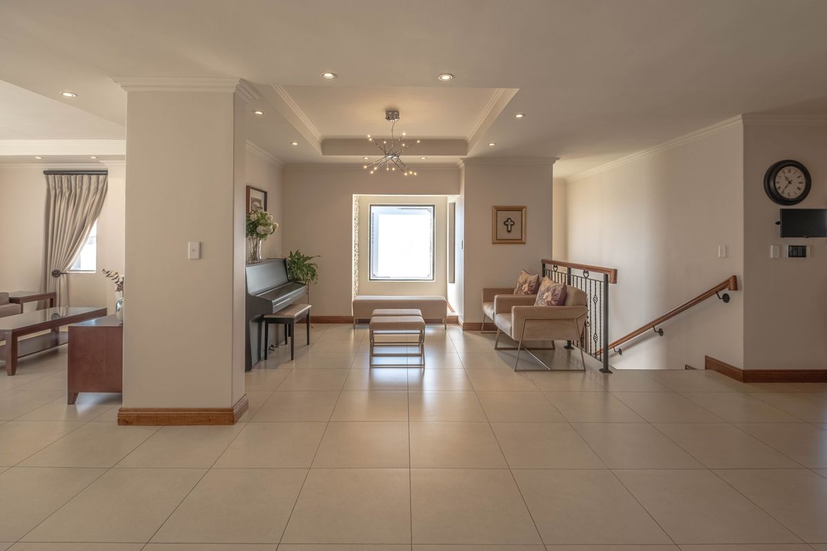 Spacious open-plan living area featuring neutral tiled flooring, recessed ceiling with downlights, and a staircase with a decorative metal railing.