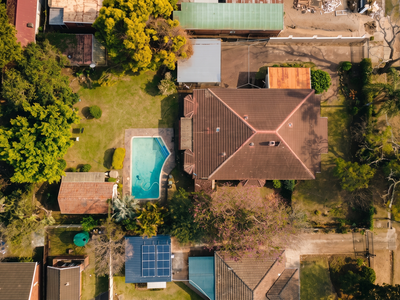 Aerial view of a residential property featuring a tiled roof house, a swimming pool, solar panels, and a spacious garden.