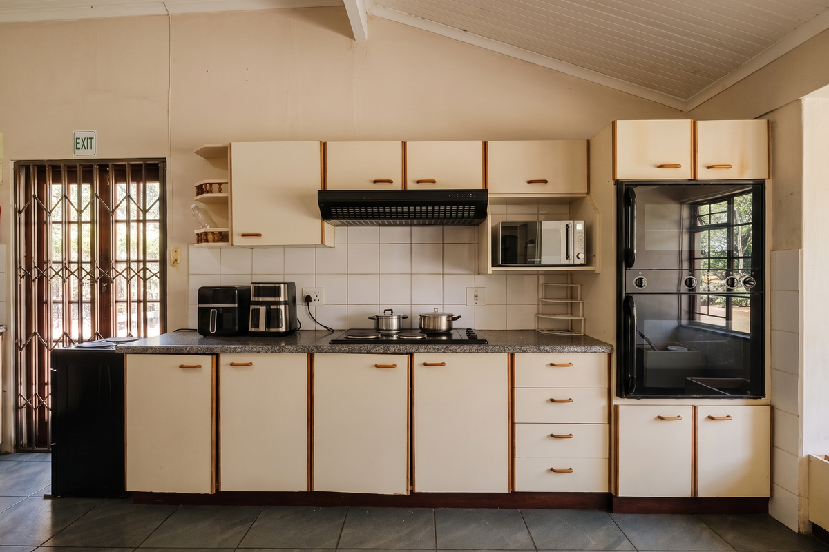 A functional kitchen featuring built-in cabinetry, an electric hob, extractor fan, and integrated oven, with direct access to an exterior security gate.