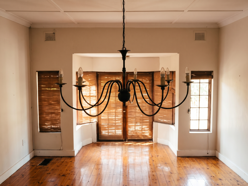An empty living room featuring polished hardwood floors, a central chandelier, and a bay window with natural light.
