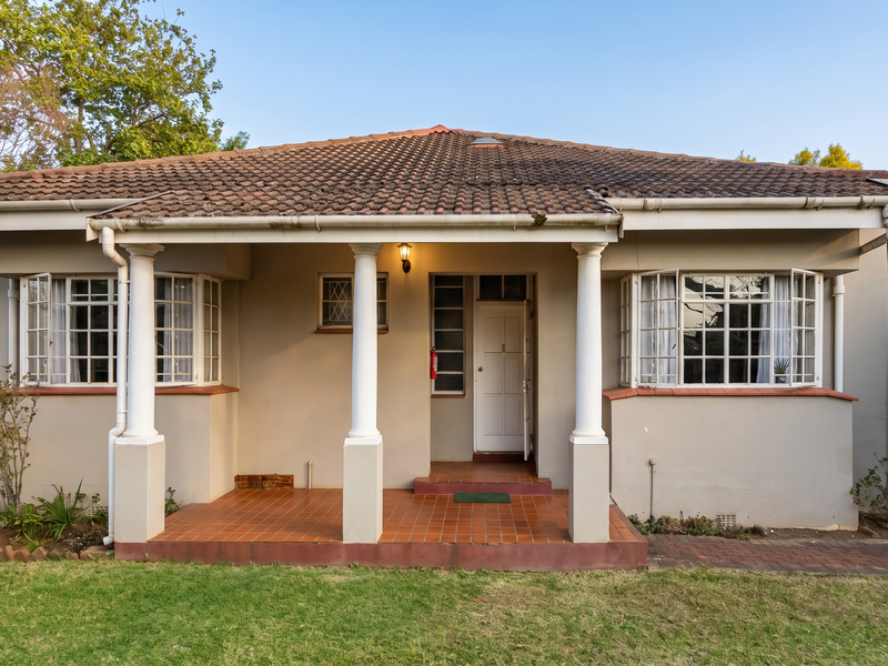 Front elevation of a single-story house featuring a covered porch with classical columns, tiled roof, and bay windows overlooking a front lawn.
