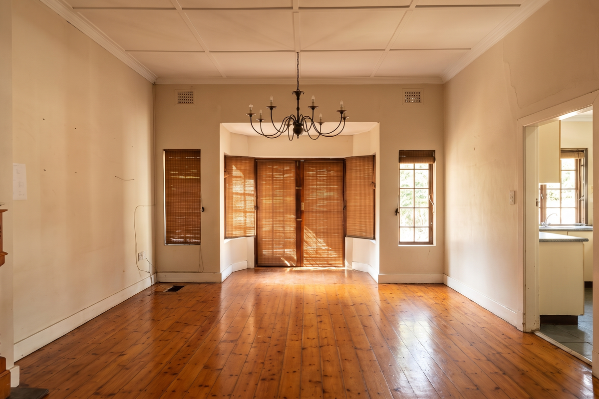 Spacious living room featuring original hardwood flooring, a classic fireplace mantel, and a bay window with natural light, offering a blank canvas for renovation.