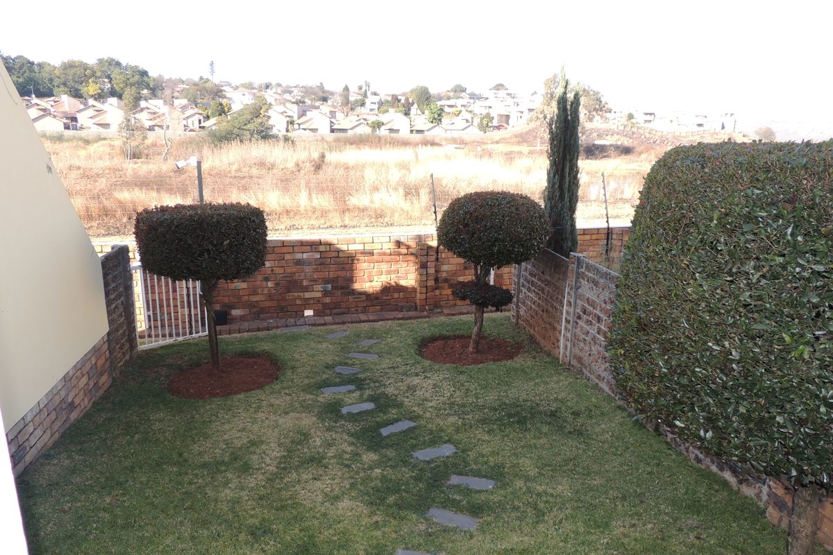 A private rear garden featuring a manicured lawn, stone pathway, and brick boundary wall with views of the surrounding neighborhood.