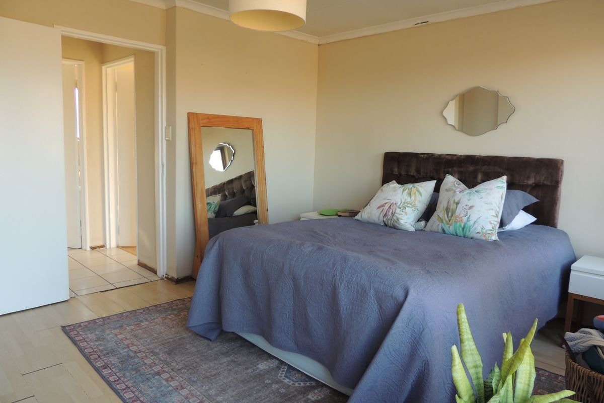 A standard bedroom featuring laminate flooring, neutral wall tones, and access to an adjoining hallway.