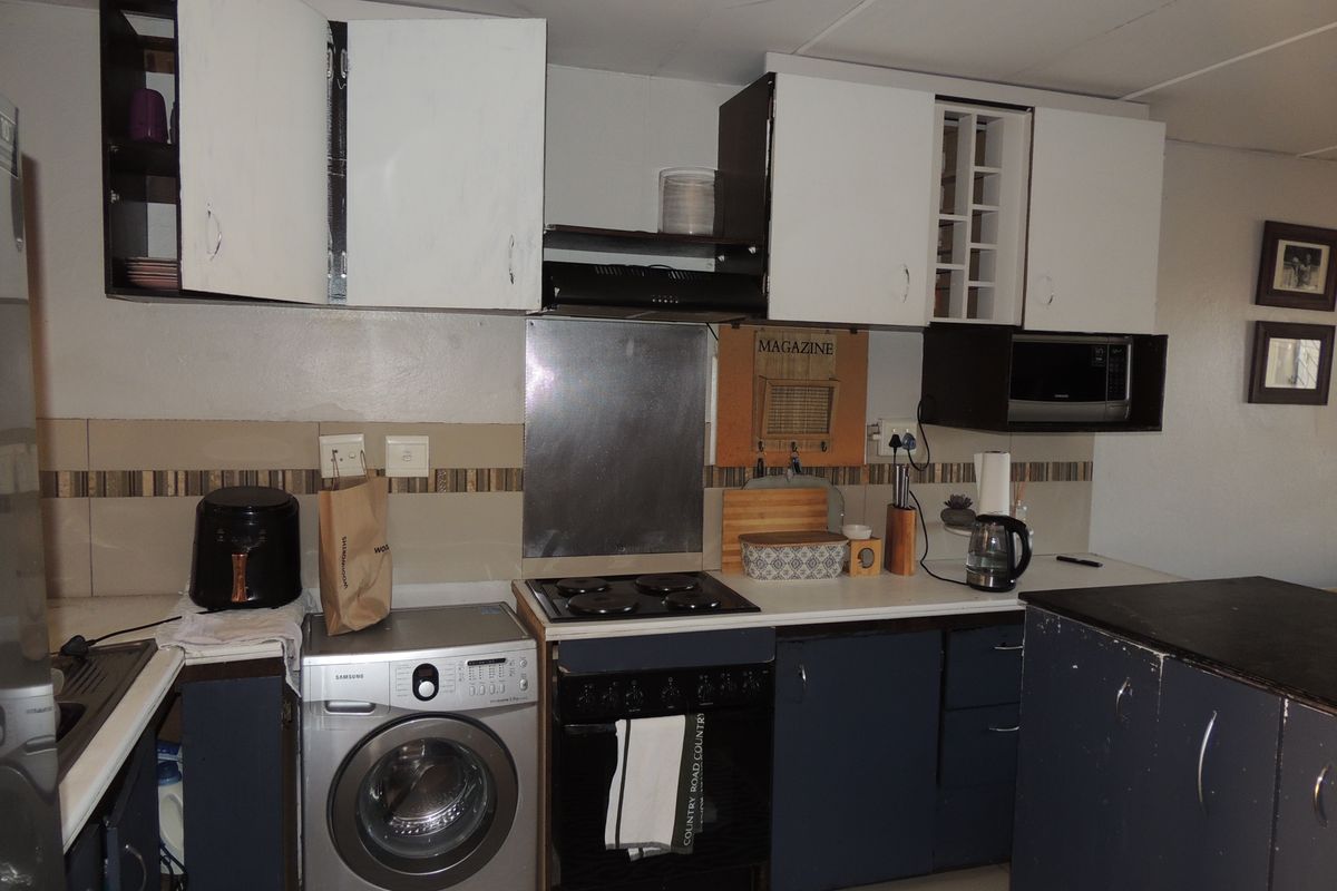 A functional kitchen featuring built-in cabinetry, an electric hob, oven, and extractor fan, with a tiled backsplash and laminate countertops.