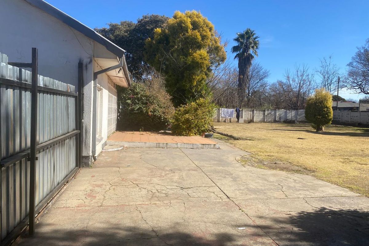 Spacious rear garden featuring a concrete patio area, tiled terrace, and established landscaping, enclosed by a combination of metal and precast concrete fencing.