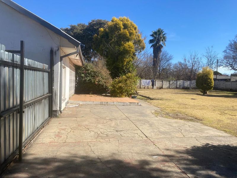Spacious rear garden featuring a concrete patio area, tiled terrace, and established landscaping, enclosed by a combination of metal and precast concrete fencing.