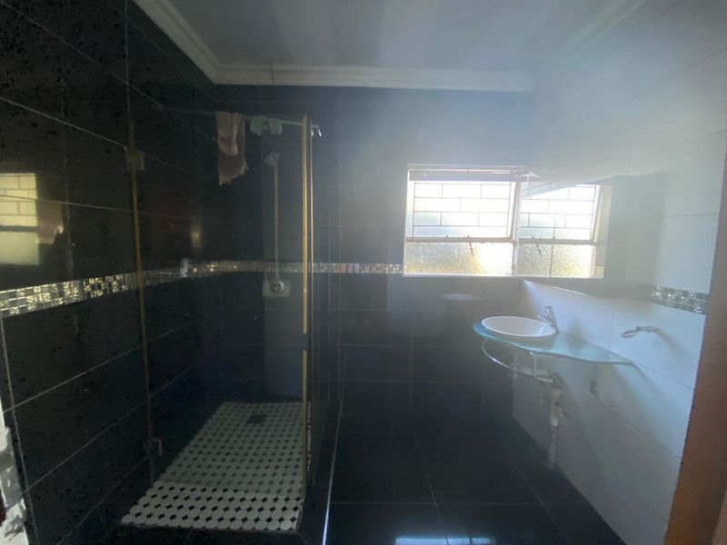 A bathroom featuring dark wall tiles, a glass shower enclosure, and a wall-mounted basin with a glass shelf.