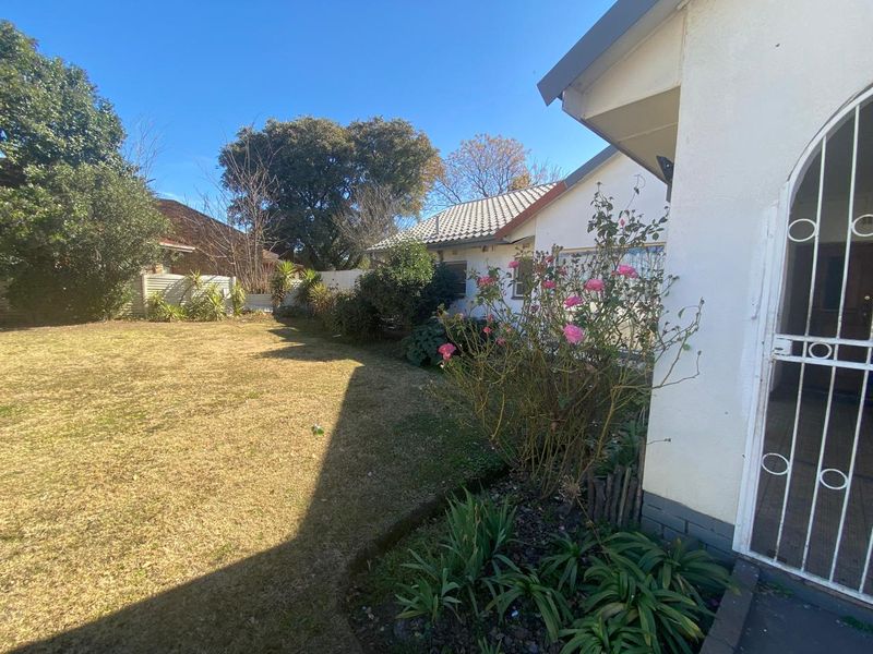 A view of the rear garden and lawn area, featuring a security gate entrance and established perimeter fencing.