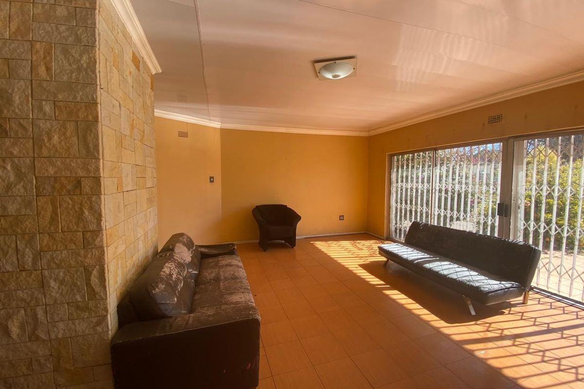 Spacious living area featuring a stone accent wall, tiled flooring, and large sliding glass doors with security gates providing access to the exterior.