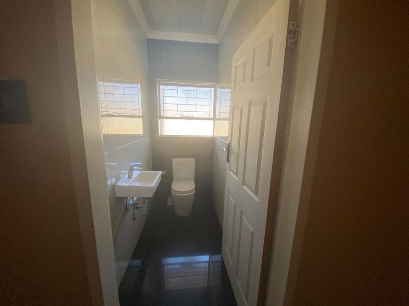 A compact, modern bathroom featuring dark floor tiles, light wall tiles, a wall-mounted basin, and a toilet.
