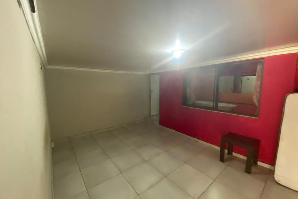 An empty bedroom featuring tiled flooring and an internal window looking into an adjacent space, requiring cosmetic updates to improve its overall appeal.