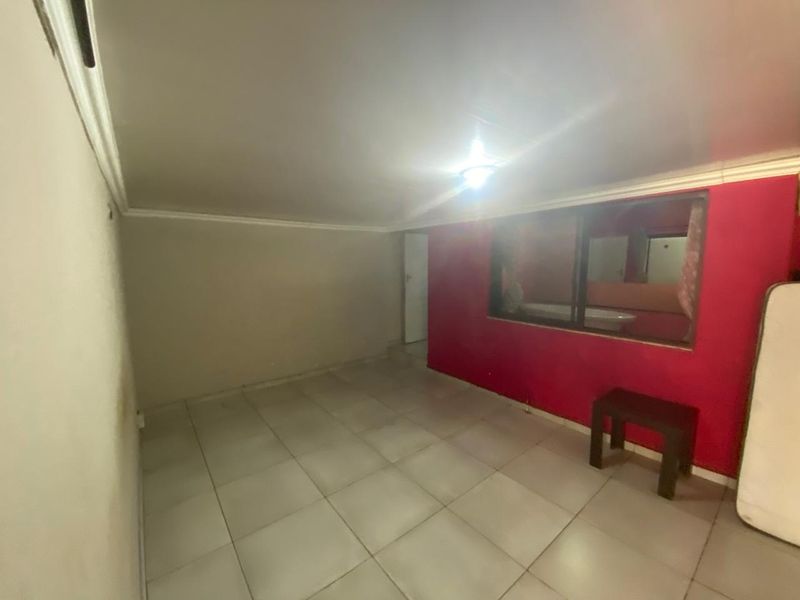 An empty bedroom featuring tiled flooring and an internal window looking into an adjacent space, requiring cosmetic updates to improve its overall appeal.
