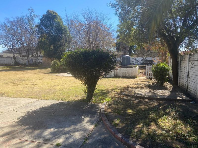 A spacious rear garden featuring a concrete patio area, established trees, and a boundary wall with a water storage tank.