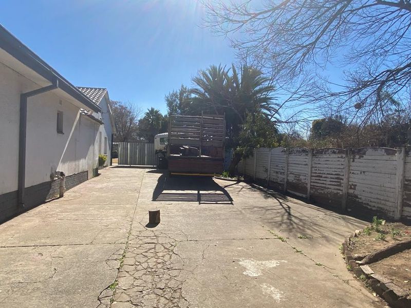A rear exterior view showing a concrete driveway, boundary walling, and side elevation of the house.