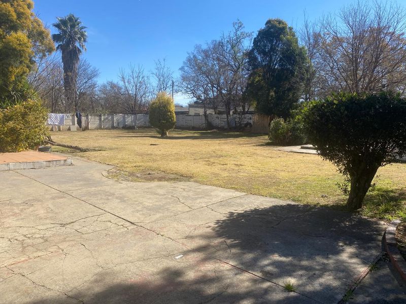 A spacious rear garden featuring a large concrete patio area with visible cracking and established perimeter fencing.