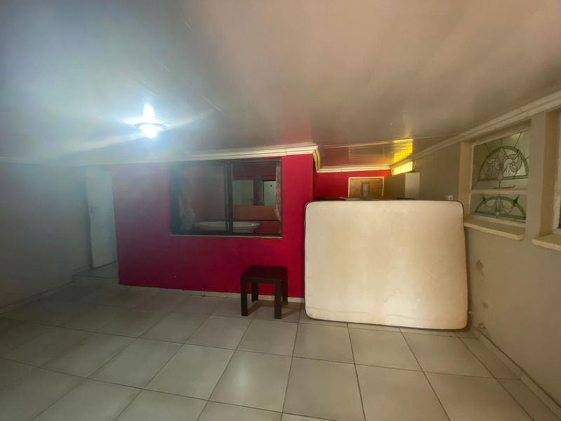 A spacious bedroom featuring tiled flooring, an internal window, and a decorative stained glass window, currently vacant and in need of cosmetic updates.