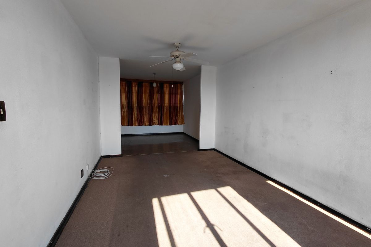 An empty, open-plan living area featuring carpeted flooring and a ceiling fan, presenting a blank canvas for potential renovation and interior design updates.
