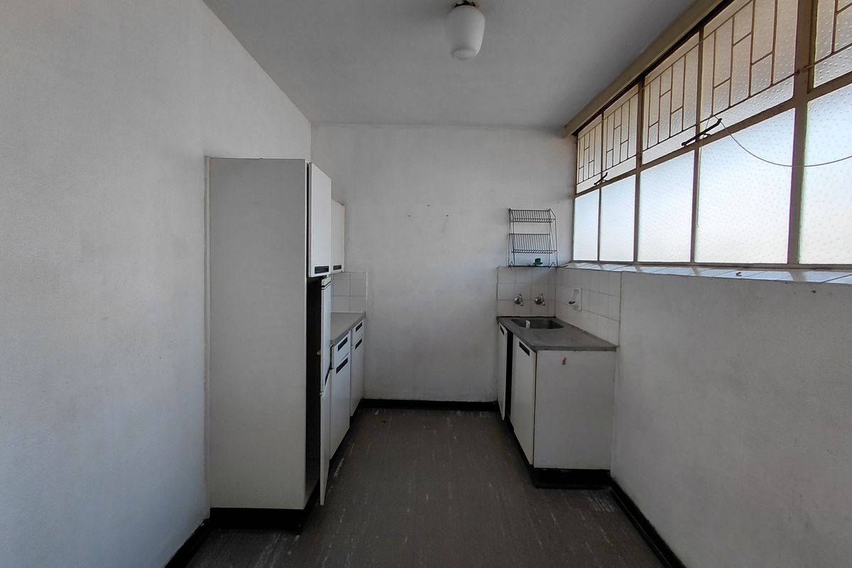 A dated, empty kitchen featuring basic built-in cabinetry, a stainless steel sink, and large clerestory windows providing natural light.