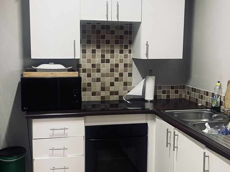 Compact kitchen featuring white cabinetry, mosaic tile backsplash, integrated oven, electric hob, and stainless steel sink with ceramic floor tiles.