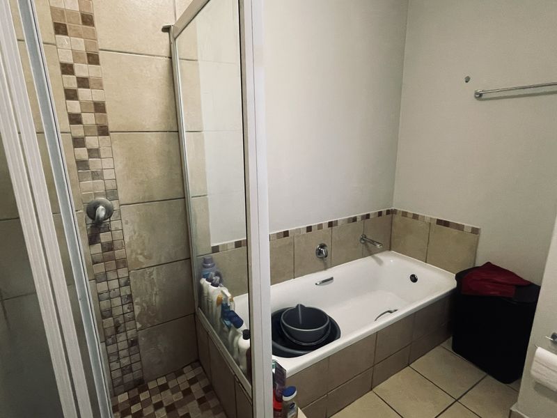A functional bathroom featuring a separate shower enclosure and a bathtub with tiled splashbacks and neutral floor tiling.